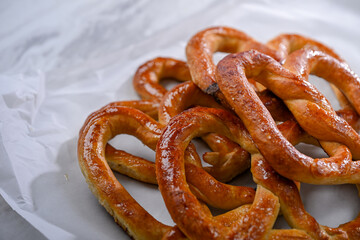 A plate of golden, freshly baked pretzels placed on a sleek white surface. The pretzels have a crispy texture on the outside and are shaped in the traditional knot, perfect for a snack or party
