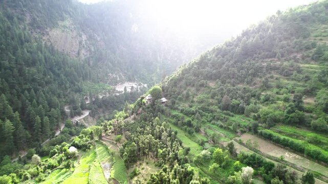 Aerial view of a small, lush village surrounded by forested hills and terraced fields in Kashmir valley