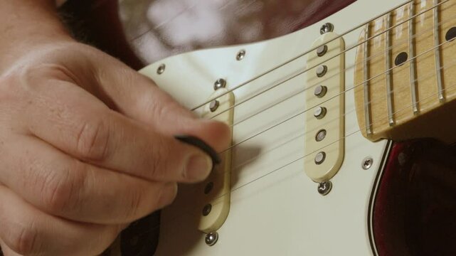 Close Up of Guitarist Hand with Plectrum Playing Deep Red Stratocaster Guitar During Band Practice Solo with Natural Light 4K