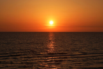 The sun setting over the horizon, casting a golden glow of the sunset across the calm waves of the Baltic sea. 