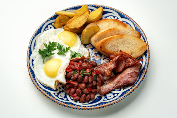 Delicious breakfast plate featuring eggs, beans, bacon, and potato wedges served on a decorative dish