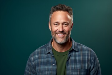 Fototapeta premium Portrait of a grinning man in his 40s wearing a comfy flannel shirt over soft green background