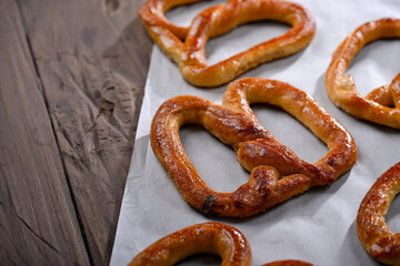 A close-up shot of freshly baked, golden-brown pretzels resting on parchment paper. The pretzels have a glossy, and the wooden background adds a rustic charm to this appetizing scene
