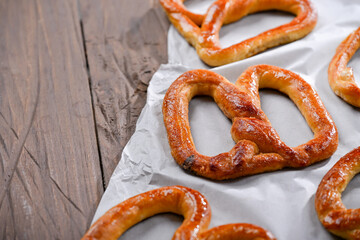 A close-up shot of freshly baked, golden-brown pretzels resting on parchment paper. The pretzels have a glossy, and the wooden background adds a rustic charm to this appetizing scene