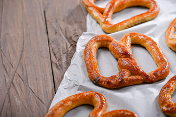 A close-up shot of freshly baked, golden-brown pretzels resting on parchment paper. The pretzels have a glossy, and the wooden background adds a rustic charm to this appetizing scene