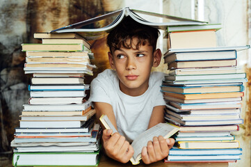 A cheerful boy looks through two stacks of books. On the head is a book in the shape of a roof
