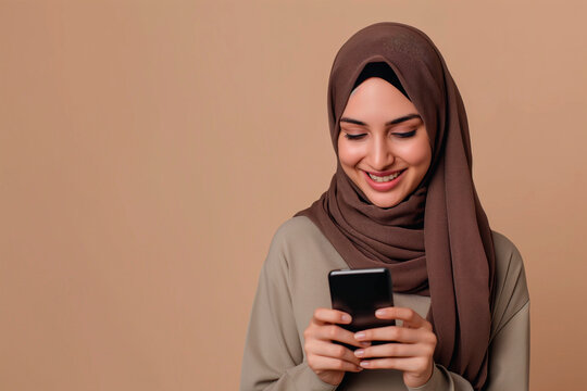 smiling muslim woman looking at her phone, commercial studio photo with plain beige background