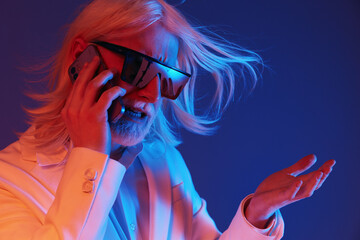 Stylish man with long white hair and sunglasses talking on the phone against a colorful background, expressing emotions with vibrant lighting and dramatic gestures