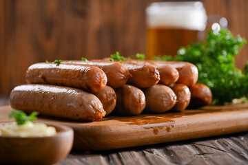 A delicious stack of grilled sausages served on a wooden board, garnished with parsley, and accompanied by a creamy dipping sauce. In the background, a frothy glass of beer
