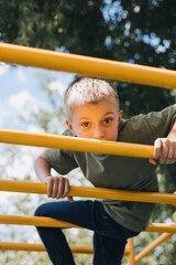 Obraz premium A school-age boy in a green T-shirt spends time on horizontal bars, a playground in sunny weather. Front view
