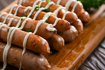 A stack of grilled sausages drizzled with creamy mayonnaise, garnished with fresh parsley. The juicy sausages are arranged beautifully on a wooden board, showcasing their smoky flavo