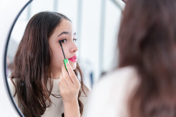 Teenage girl applying makeup, young girl putting some mascara on her eyelashes in front of a mirror