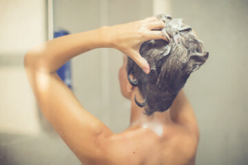 Naklejka premium Woman in shower rinse shampoo foaming with water dripping on hair and body. Taking shower relaxing under warm running water. Female washing her hair and hand to massage head while washing hair.