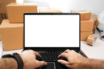 A laptop with a blank white screen on a table is being used by a seller to answer product orders online , ecommerce online market concept