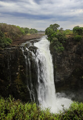 Fototapeta premium Majestic view of Victoria Falls cascading over cliffs in Zimbabwe during cloudy weather