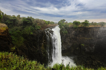 View of Victoria Falls cascading from the cliffs surrounded by lush greenery in Zimbabwe during a bright, sunny day