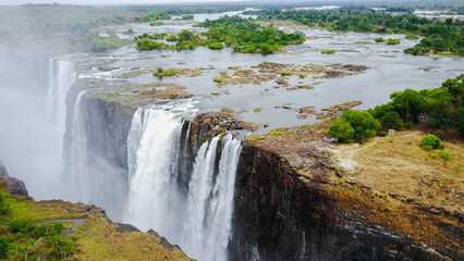 Victoria Falls cascading dramatically over cliffs in Zimbabwe with lush greenery surrounding the water and distant landscapes at dawn © Dave