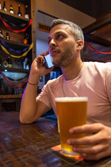 A man is talking on his cell phone while holding a glass of beer