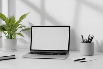 Fototapeta premium A laptop with a blank screen on a clean, minimalist desk setup, featuring a potted plant and a cup of pencils, bathed in natural sunlight casting soft shadows