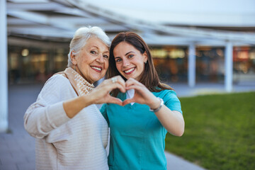 Joyful Senior Woman and Caregiver Making Heart Shape Outdoors