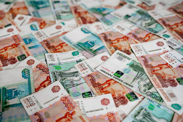 Russian money rubles with a denomination of one thousand rubles and five thousand rubles lie on the entire background of the image, green and expensive