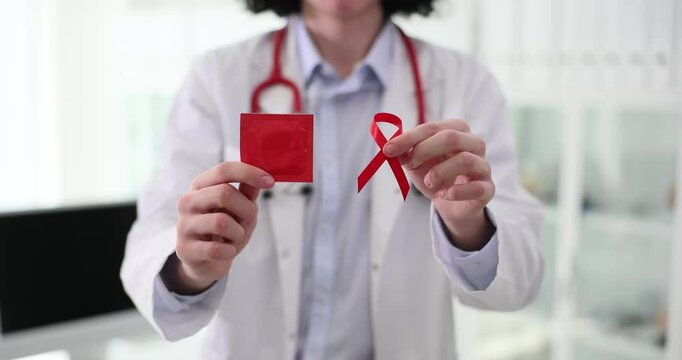 Doctor with red ribbon and condom in hand closeup. Contraceptive methods for HIV positive patients concept