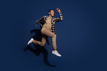 Obraz premium Full length photo of cheerful positive guy dressed plaid shirt jumping high running emtpy space isolated blue color background