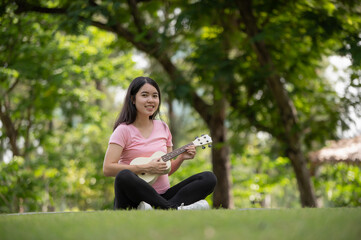Obraz premium Asian healthy pregnant woman enjoying and relaxing by playing Ukulele in the park, Music time