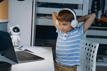 caucasian little boy studying at home sitting at the desk stretching hands up