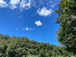 鮮やかな青空とふんわりとした白い雲、そして緑のスペースが特徴的な背景で、テキストやデザイン要素に最適です