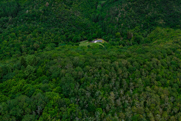 A house in a green forest valley among mountains and hills. The concept of living far from civilization.