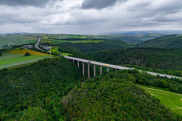 Obraz premium cargo trucks on the highway on the bridge. asphalt road among green forest and beautiful rain clouds. cargo delivery and transportation concept