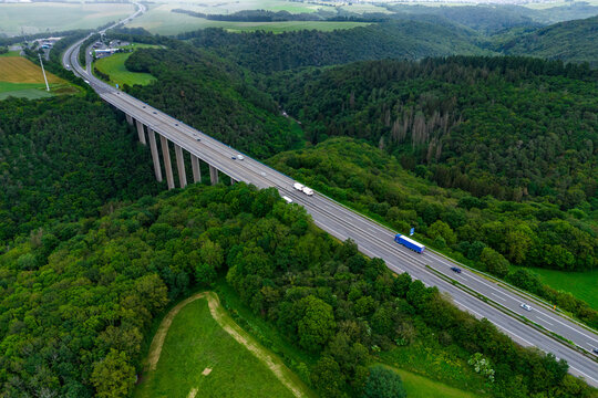 blue cargo truck and cars on the highway on the bridge. asphalt road among green forest and beautiful rain clouds. cargo delivery and transportation concept