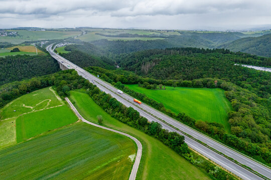 orange cargo truck and cars on the highway. asphalt road among green forest and beautiful rain clouds. cargo delivery and transportation concept