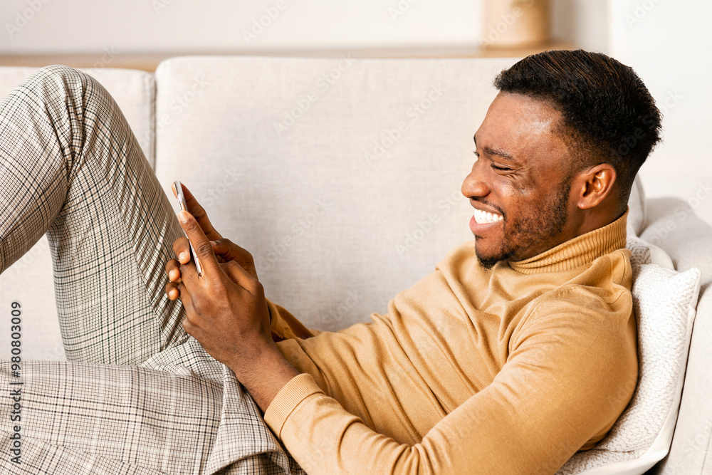 Poster mobile app. relaxed black guy using smartphone playing games lying on sofa at home.