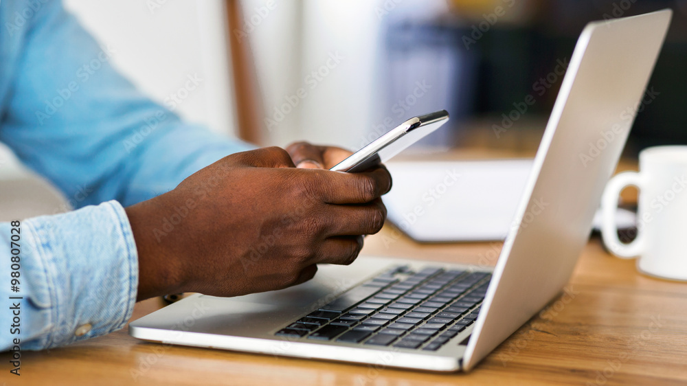 Aufkleber Multitasking concept. Unrecognizable african american employee typing message on smartphone and working with laptop in office, side view with copy space
