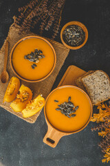Two bowls of pumpkin puree soup with meatballs, pumpkin seeds, a sprig of rosemary, horizontal on a dark background