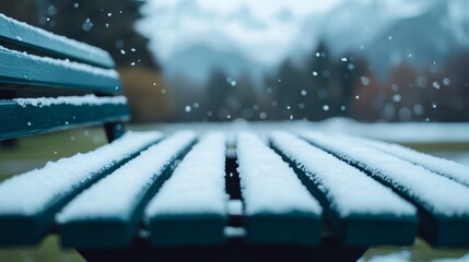 Flakes of snow settling on an outdoor bench and table, light dusting accumulating, and winter chill visible 