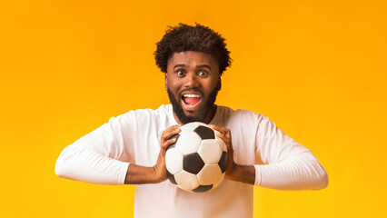 Excited african american football fan with ball on orange background, copy space