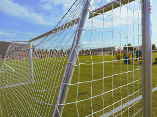 Close-up of goal net with players in uniform in background. Training on soccer field