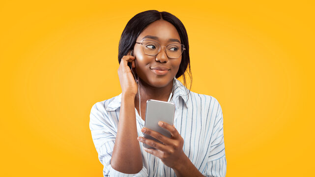 African American Girl Using Phone And Earphones Listening To Audio Book Standing On Pink Background. Studio Shot