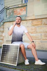 Handsome man using smartphone connected to photovoltaic solar panel. Integration of sustainable...