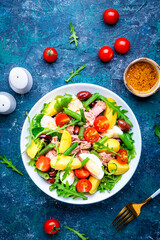 French gourmet salad with tuna, tomatoes, eggs, beans, potatoes and olives on blue background, top view