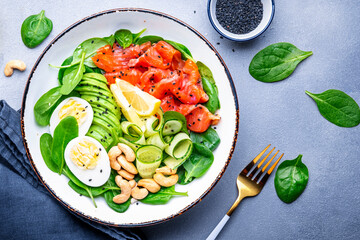 Keto diet salad with salmon, avocado, spinach, eggs and cashew. Gray table background, top view