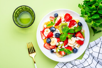 Fruit and berry salad with ricotta and honey, green background, top view