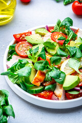 Fresh salad with avocado, chicken, tomatoes and lettuce, gray background, top view