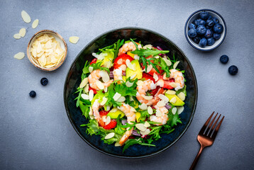 Shrimp salad with strawberries, onions, lettuce and almonds, gray background, top view