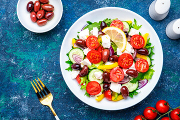 Greek salad with feta cheese, olives, tomatoes, lettuce, paprika, cucumber and onion. Blue background, top view