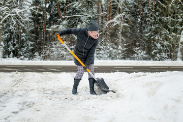 Naklejka premium Mature woman shoveling snow in a backyard on winter day.