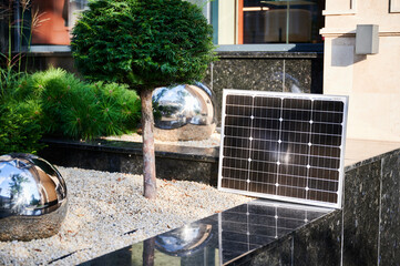 Photovoltaic solar panel against backdrop of vibrant green trees on stone ledge, soaking up...